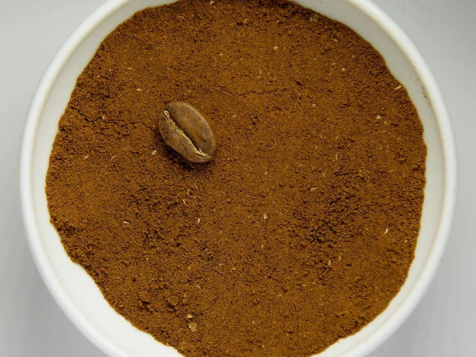 Fein gemahlenes Kaffeepulver in einer weißen Schale mit einer ganzen Bohne